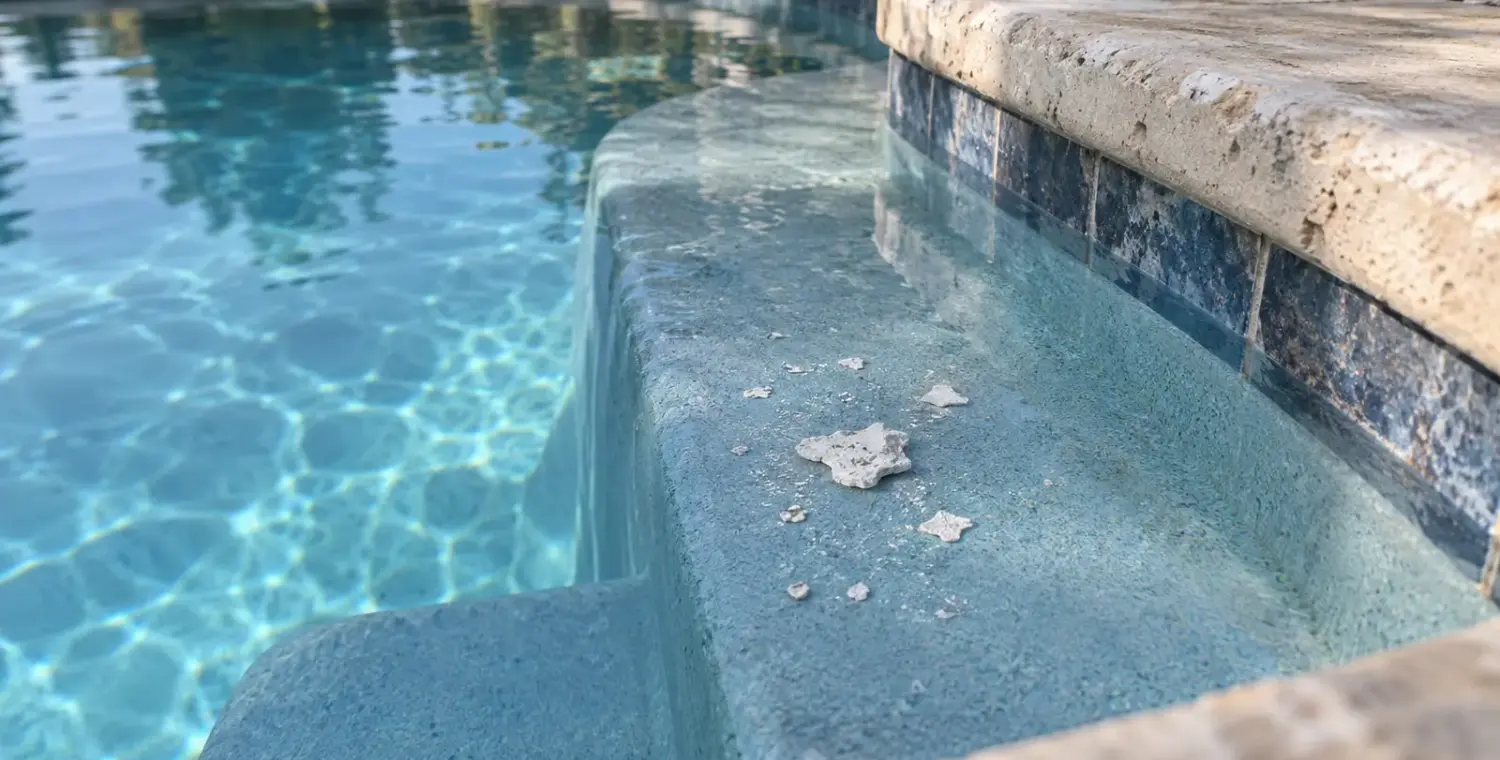 Irregular white flakes rest on a shallow blue pool step beside light stone coping.